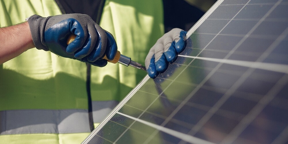 mãos de um funcionário com uma chave de fenda realizando a fixação de um parafuso de uma placa de energia solar fotovoltaica