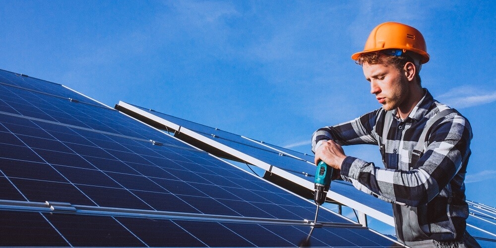 funcionário de uma empresa de instalação de energia solar com uma furadeira na mão apertando um parafuso de fixação de uma placa fotovoltaica