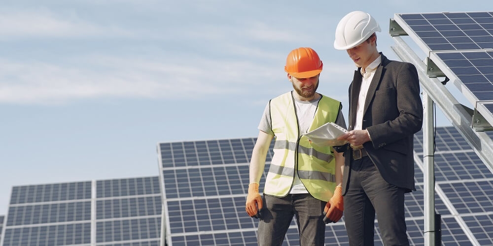 engenheiro com a camisa preta ao lado de um instalador de energia solar com a camisa verde analisando pontos de instalação das placas fotovoltaicas