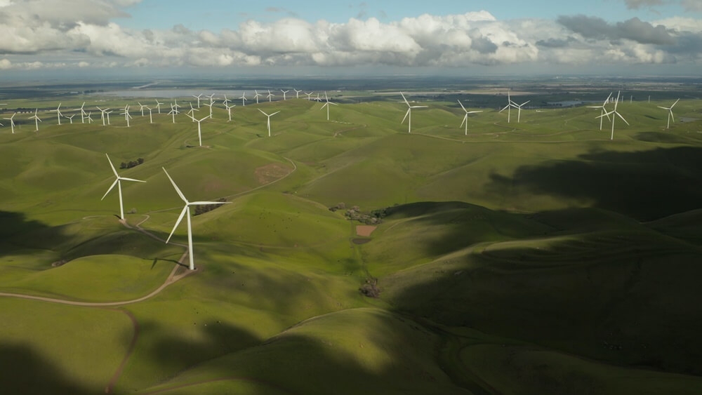 várias torres de turbina eólica entre uma paisagem verde e montanhosa no Brasil