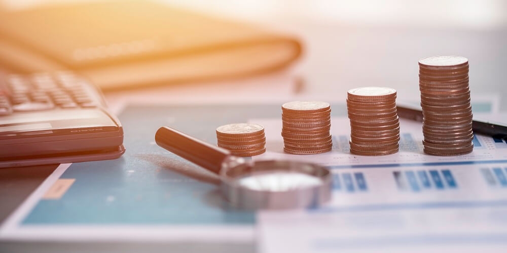 calculadora, lupa e moedas sobre uma folha contendo impostos relacionados à taxação do sol