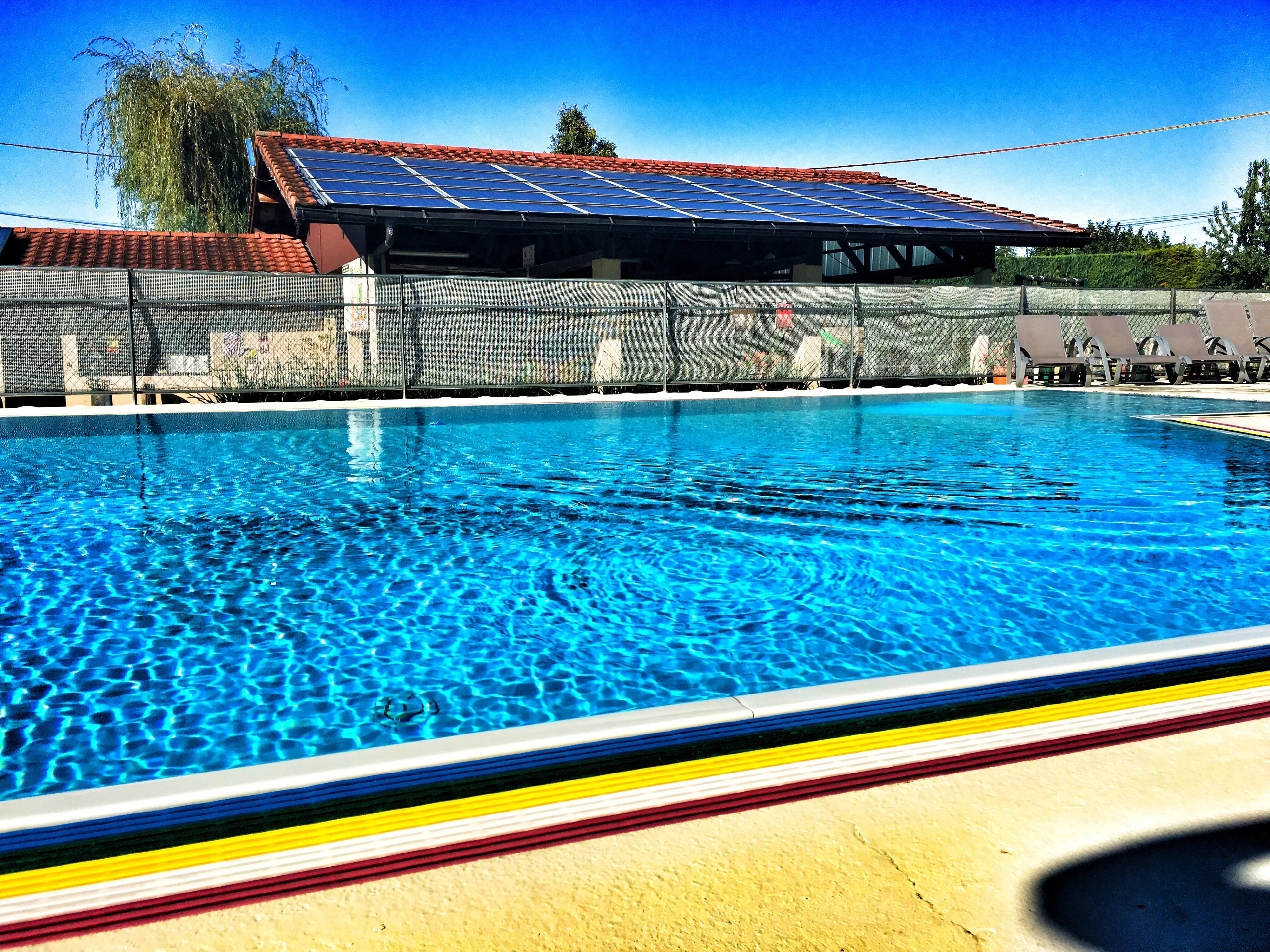 uma piscina e logo ao fundo várias placas de energia solar fotovoltaica