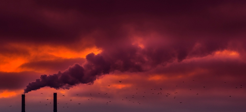 chaminés industriais emitindo fumaça contra um céu dramático com nuvens densas e coloração intensa