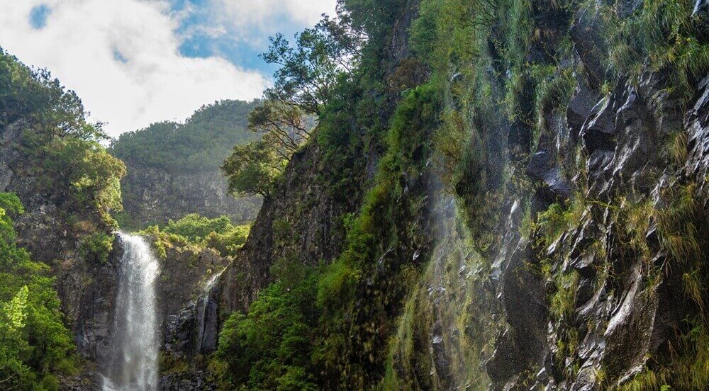 paisagem natural com uma cachoeira fluindo e ao lado várias montanhas rochosas e o céu azul