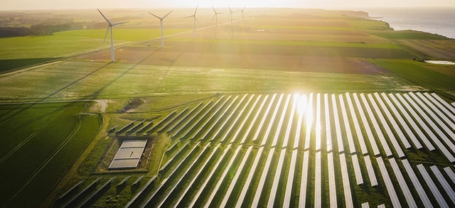 foto aérea de uma grande área verde com diversas placas de energia solar fotovoltaica e torres de energia eólica