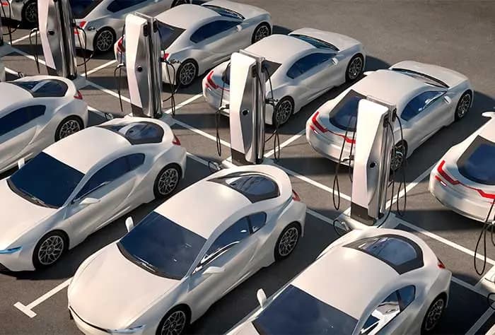 ESTACIONAMENTO COM VÁRIOS CARROS ELÉTRICOS BRANCOS CONECTADOS A CARREGADORES