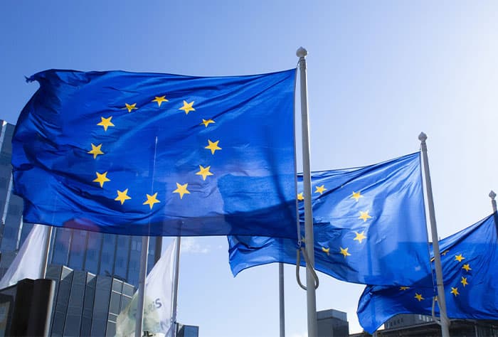 BANDEIRAS DA UNIÃO EUROPEIA TREMULANDO AO VENTO EM FRENTE A EDIFÍCIOS MODERNOS, SOB CÉU AZUL