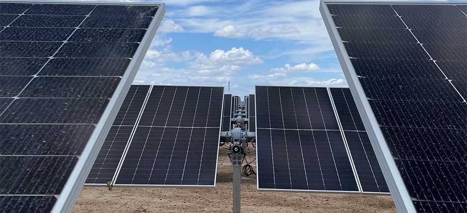 PAINÉIS SOLARES BIFACIAIS INSTALADOS EM ESTRUTURA COM SEGUIDOR SOLAR EM CAMPO ABERTO, SOB CÉU AZUL COM NUVENS