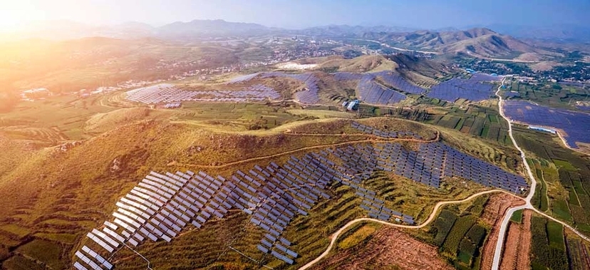 PARQUE SOLAR DE GRANDE ESCALA INSTALADO EM ÁREA MONTANHOSA NA CHINA, COM MILHARES DE PAINÉIS FOTOVOLTAICOS COBRINDO AS COLINAS, SOB CÉU LIMPO AO ENTARDECER