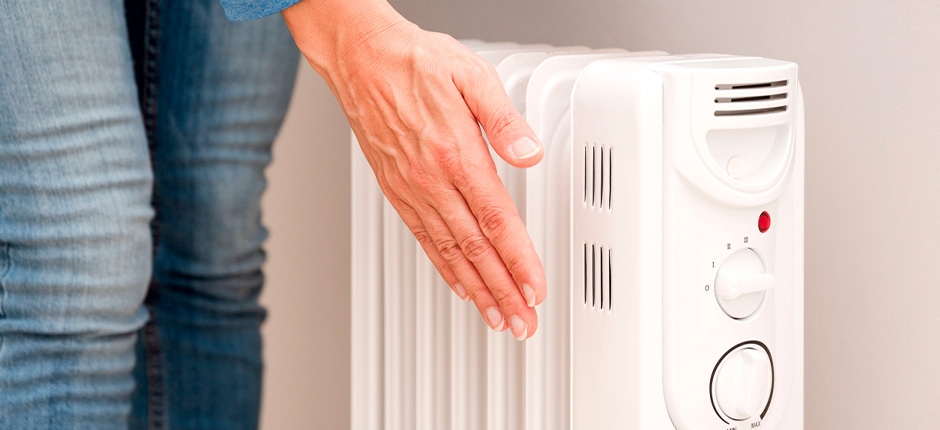 PESSOA APROXIMANDO A MÃO DE UM AQUECEDOR ELÉTRICO PORTÁTIL LIGADO