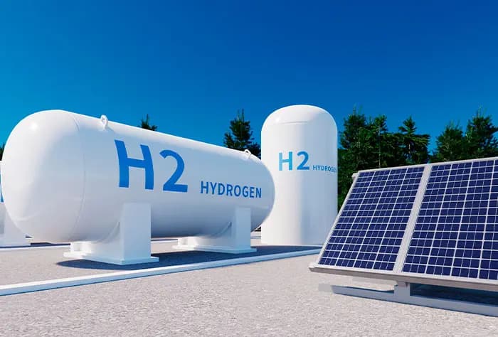 TANQUES BRANCOS DE ARMAZENAMENTO DE HIDROGÊNIO COM A INSCRIÇÃO "H2 HYDROGEN" AO LADO DE PAINÉIS SOLARES EM UM AMBIENTE EXTERNO ENSOLARADO
