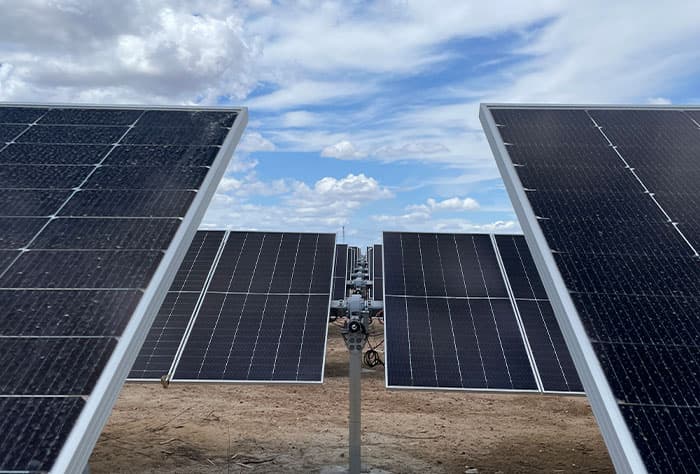 PAINÉIS SOLARES BIFACIAIS INSTALADOS EM ESTRUTURA COM SEGUIDOR SOLAR EM CAMPO ABERTO, SOB CÉU AZUL COM NUVENS