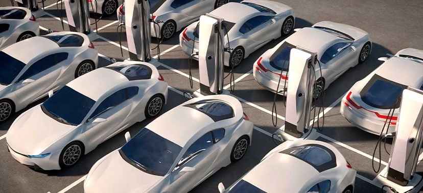 ESTACIONAMENTO COM VÁRIOS CARROS ELÉTRICOS BRANCOS CONECTADOS A CARREGADORES