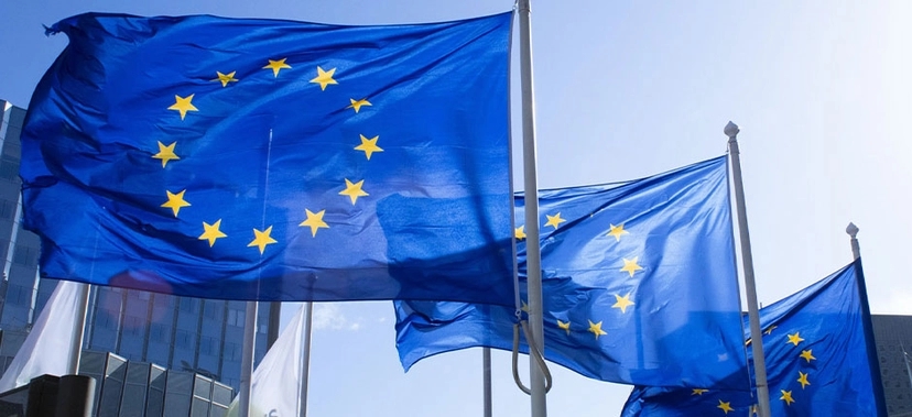 BANDEIRAS DA UNIÃO EUROPEIA TREMULANDO AO VENTO EM FRENTE A EDIFÍCIOS MODERNOS, SOB CÉU AZUL