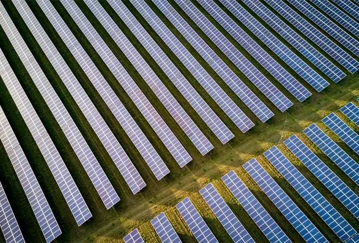 VISTA AÉREA DE UMA USINA SOLAR COM FILEIRAS DE PAINÉIS FOTOVOLTAICOS INSTALADOS EM UM CAMPO