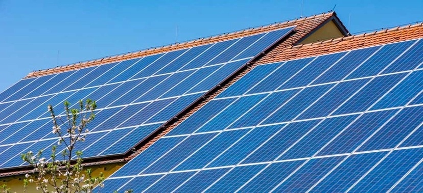 PAINÉIS SOLARES INSTALADOS NO TELHADO DE UMA CASA SOB CÉU AZUL, REPRESENTANDO O USO DE ENERGIA SOLAR RESIDENCIAL