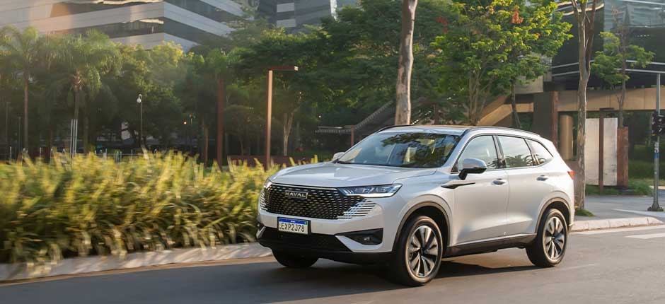 SUV HÍBRIDO HAVAL H6 ESTACIONADO EM FRENTE A UM PRÉDIO COM JARDIM