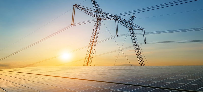 campo de painéis solares com um grande poste de transmissão de energia elétrica ao fundo