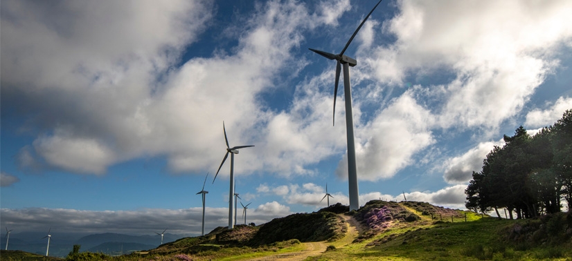 parque eólico, com várias turbinas eólicas posicionadas em uma colina verde, sob um céu parcialmente nublado