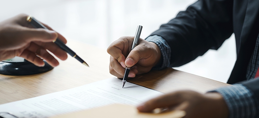 Duas pessoas assinando um papel em financiamento com caneta nas mãos