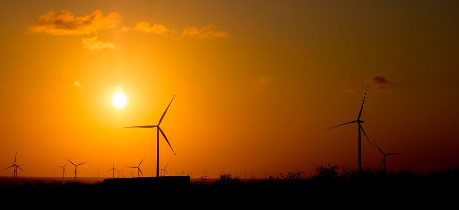 cenário ao pôr do sol onde várias turbinas eólicas estão espalhadas por uma paisagem sendo eles alguns exemplos de recursos energéticos