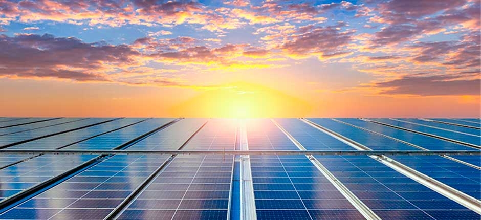 placas solares e ao fundo um por do sol com um cel azul, cheio de nuvens e alaranjado