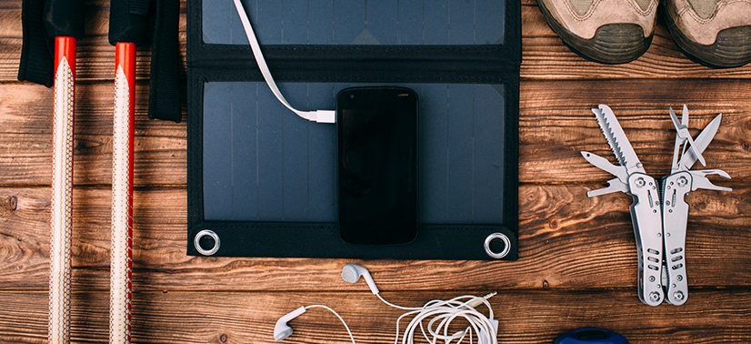 mesa com preparativos para camping e um carregador solar conectado a um celular