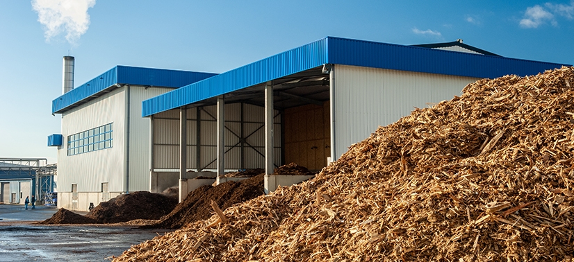 grande pilha de biomassa em frente a um prédio industrial com uma chaminé