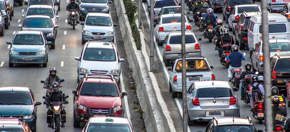 trânsito repleto de carros e motos soltando fumaça, que contribui para o efeito estufa