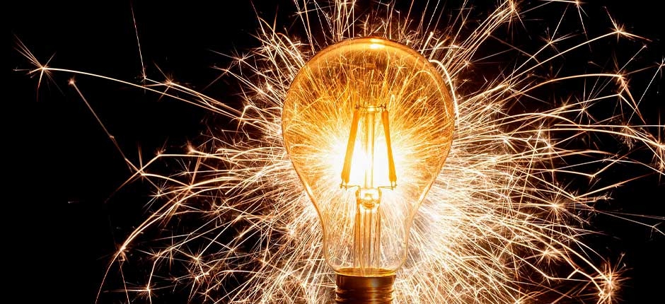 LÂMPADA INCANDESCENTE BRILHANDO INTENSAMENTE, COM FAÍSCAS AO REDOR DELA