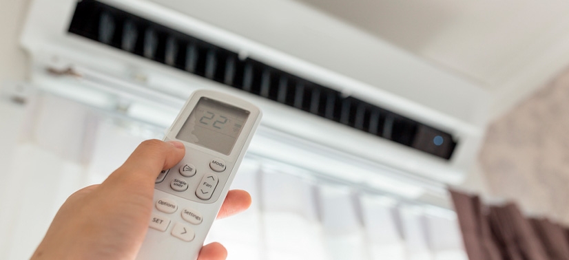 mão de uma pessoa segurando um controle de ar condicionado com selo procel e ligando ele em uma temperatura de 22º