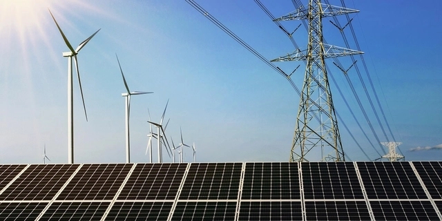 na frente várias placas de energia solar fotovoltaica e ao fundo torres de energia eólica e uma grande torre de energia elétrica