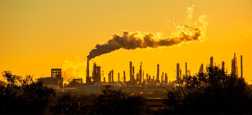 várias chaminés soltando fumaça e ao fundo a cor de um céu amarelo