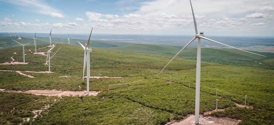 várias turbinas eólicas posicionadas em um terreno ondulado e um céu parcialmente nublado