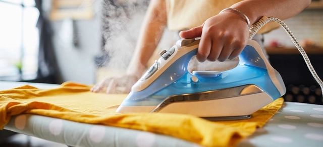 pessoa com um ferro de passar roupa realizando o procedimento em uma blusa amarela