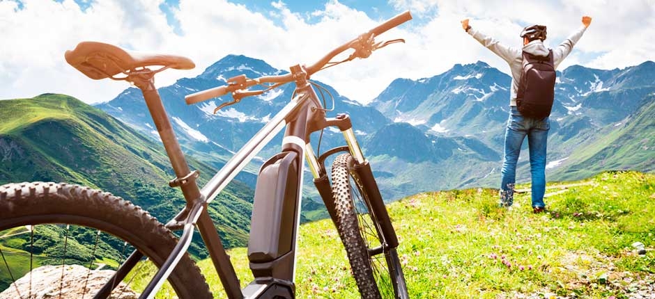bicicleta elétrica na frente e ao fundo uma linda paisagem montanhosa e uma pessoa com os braços para o alto