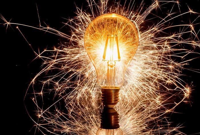 LÂMPADA INCANDESCENTE BRILHANDO INTENSAMENTE, COM FAÍSCAS AO REDOR DELA