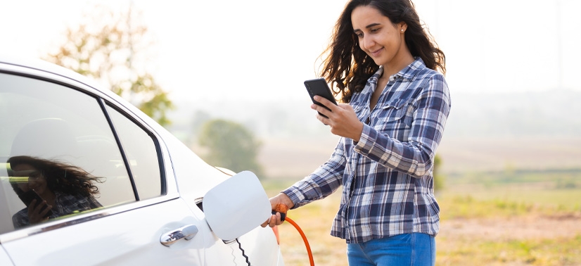 Mulher na rua carregando seu carro descobrindo quanto tempo demora para carregar carro elétrico